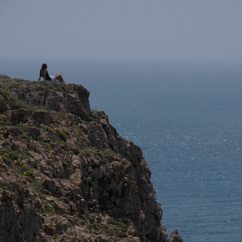Person sitting on cliff overlooking the ocean